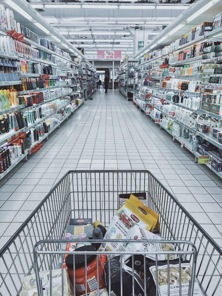 Wózek sklepowy z produktami w środku, przemierzający alejki supermarketu.