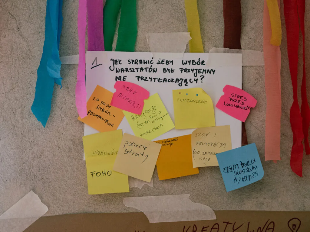 Kartka z pytaniem: 1. Jak moglibyśmy sprawić, by wybór warsztatów był przyjemny, a nie przytłaczający? I kilka pasujących do tego pytania kartek z tablicy empatyzacji.